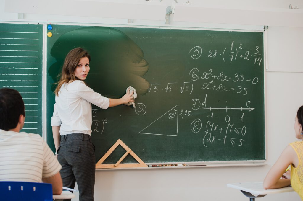 Female teacher at high school washes the chalkboard and lookng to the people in class